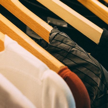 A close-up view of a row of clothes on wooden hangers, showcasing various fabrics and colors in a wardrobe setting.